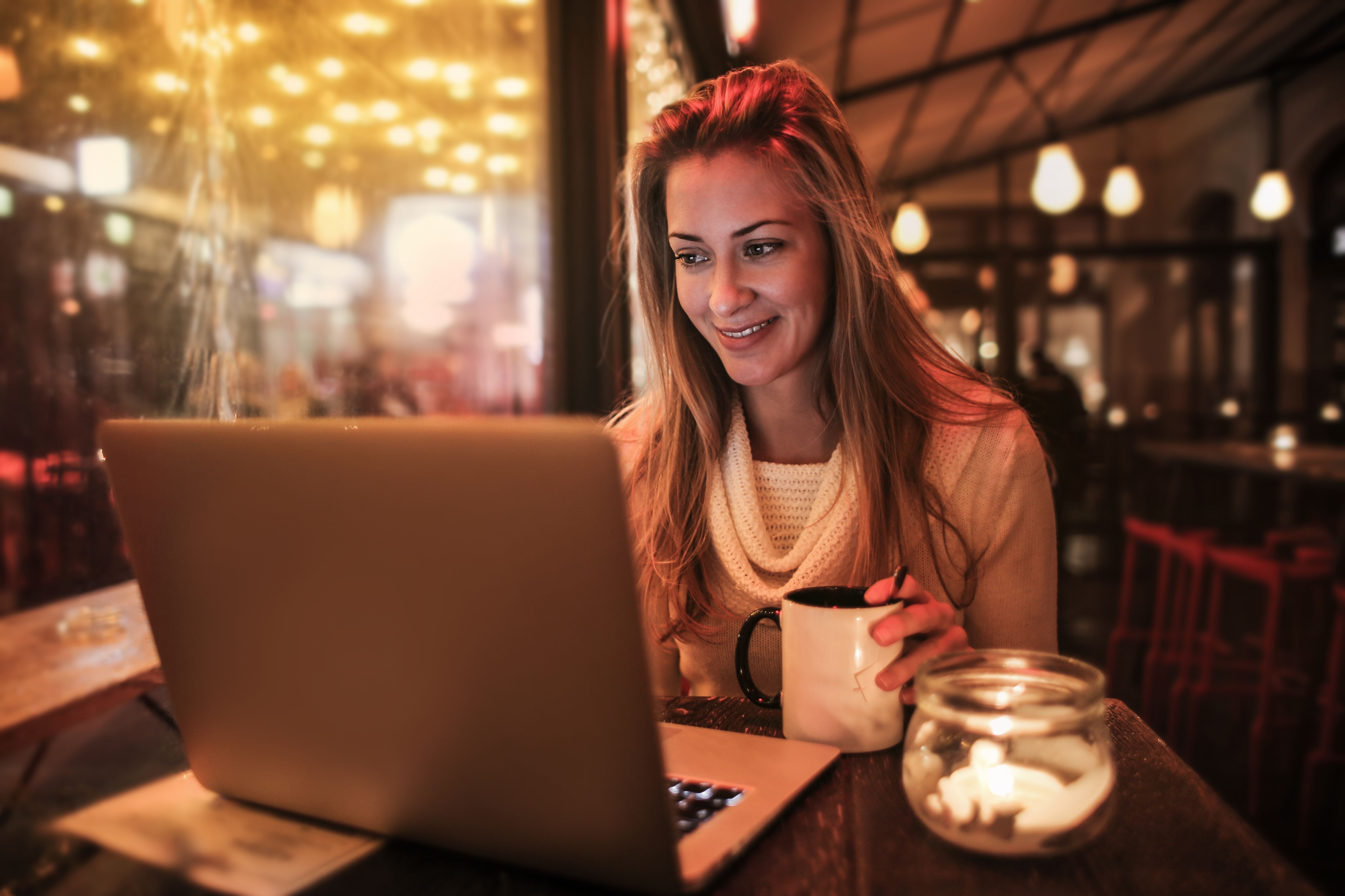 Step2Love woman in a cozy sweater using a laptop at a cafe with a cup of coffee.